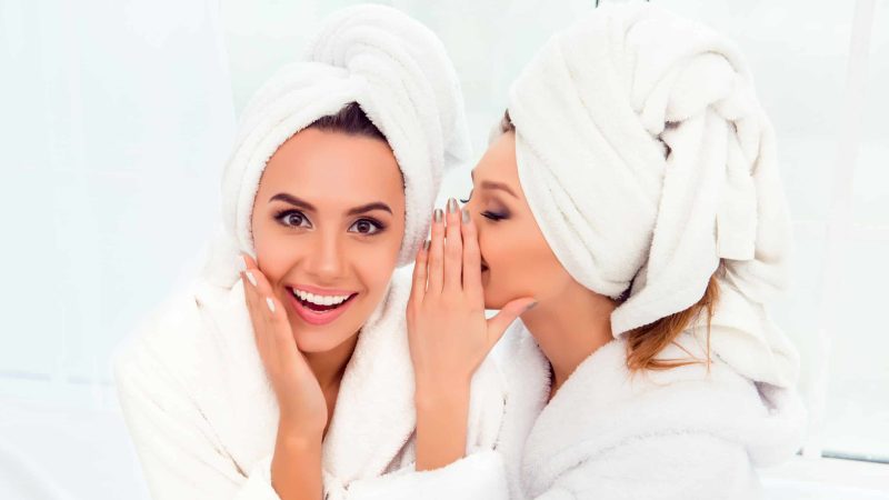 Girl in bathrobe and  towel on her head telling secret to her si Girl in bathrobe and  towel on her head telling secret to her sister
