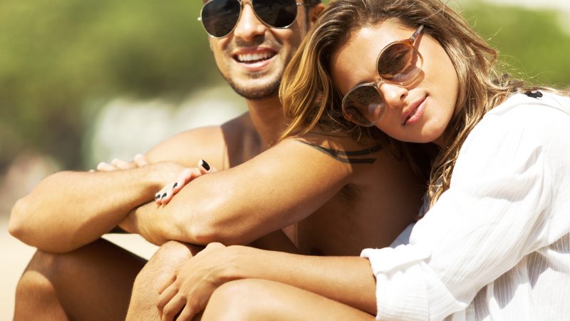 Happy young couple sitting on the beach enjoying warm sun.